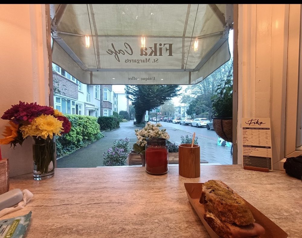 The view out through Fika Cafe's front window from the wooden counter, with flowers, sauce bottles and a loaf cake on a board